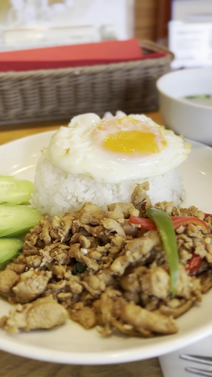 白い皿に盛ったガパオライス。ご飯の上に目玉焼き、手前に鶏ひき肉の炒め物と赤と緑のピーマン、左にきゅうりの薄切り。