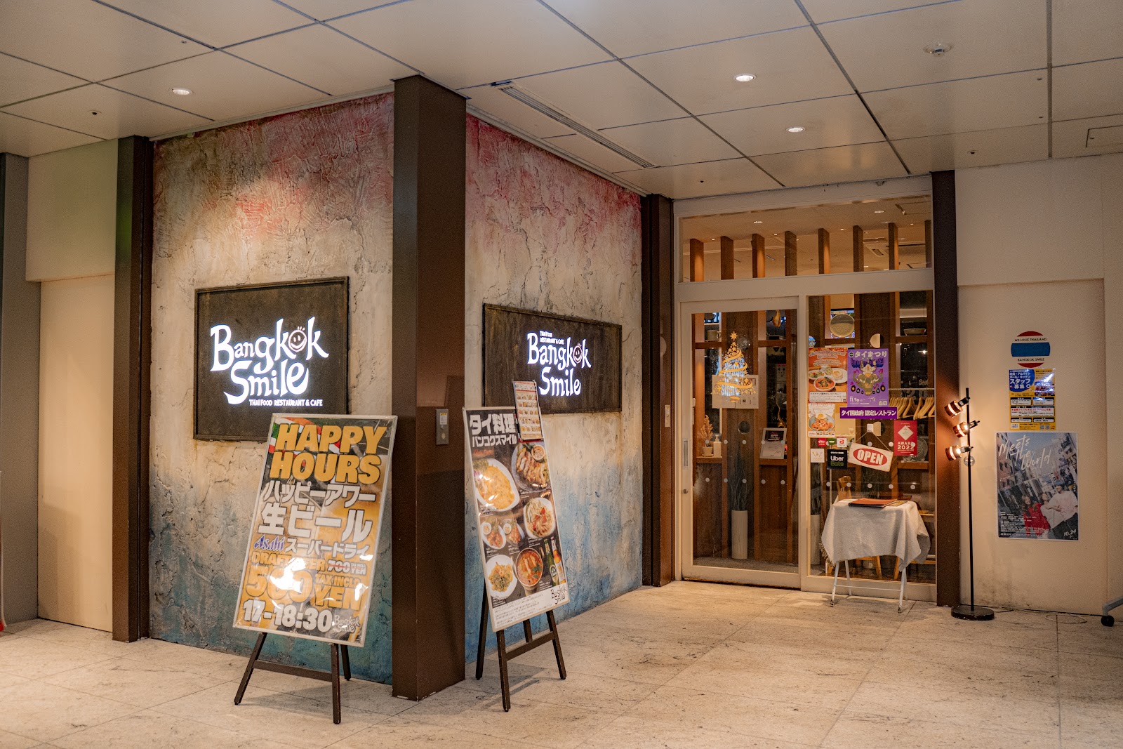 バンコクスマイルの店先。赤と青に塗られた壁に店名の看板、木枠のガラス戸、その脇に白いクロスをかけた小さなテーブル。